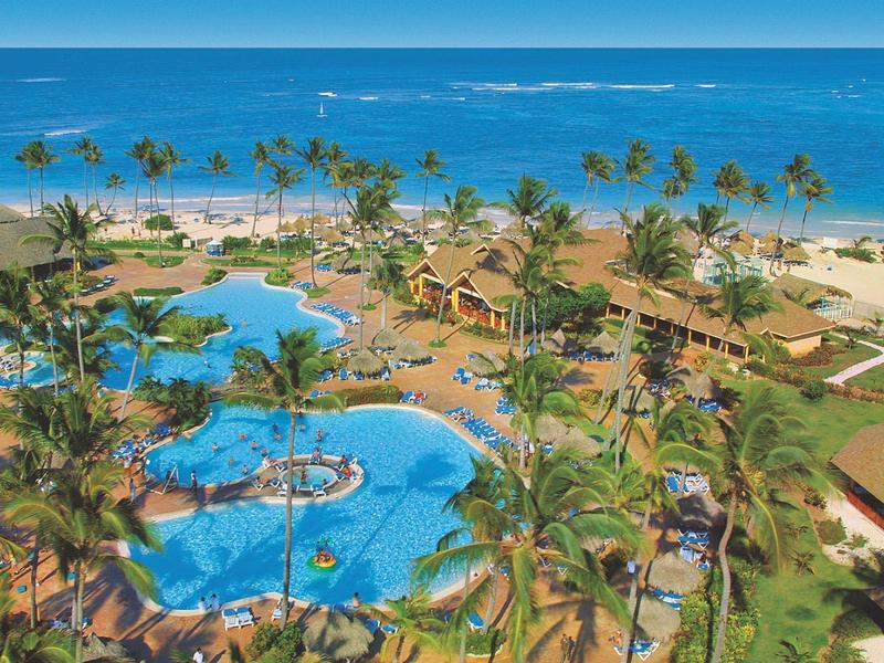 Resort with multiple pools and palm trees by the beach overlooking the sea.