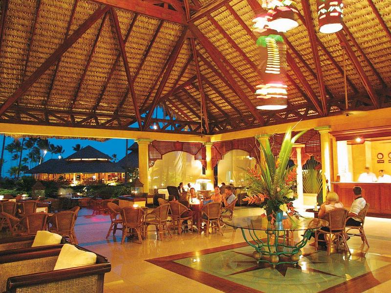 Open tropical hotel lobby with wooden ceiling, seating areas, and evening sky view