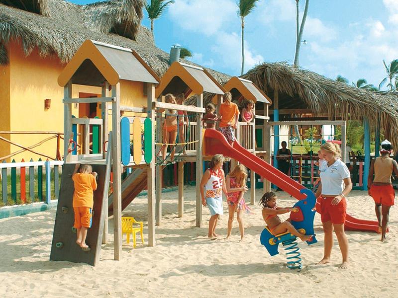 Children playing on a colorful playground with slide and climbing frame in sand under blue sky.
