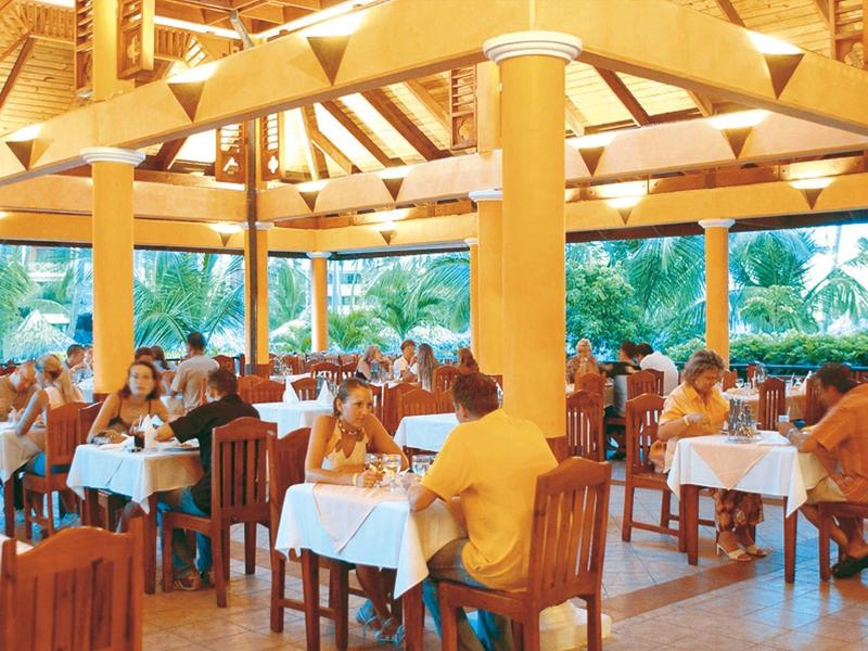 Open dining area with wooden furniture and white tablecloths, tropical surroundings visible.