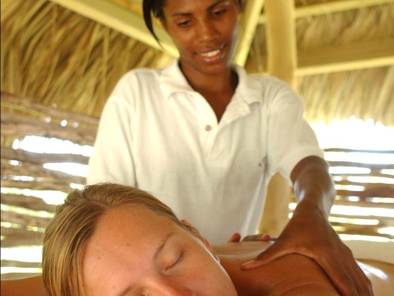 A woman receives an outdoor massage under a thatched roof.