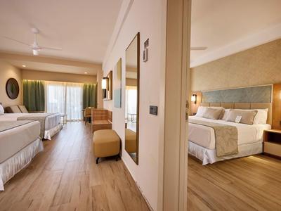 Bright hotel rooms with wooden flooring, two beds, and modern decor, separated by a wall.
