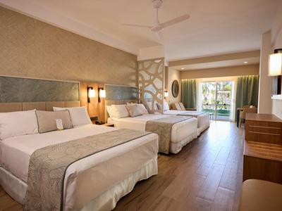 Bright hotel room with two large beds and balcony overlooking garden.