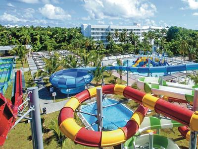 Water park with slides and pools in front of a hotel under blue sky.