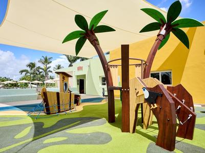 Colorful kids' playground with palm trees and a water park in the background.