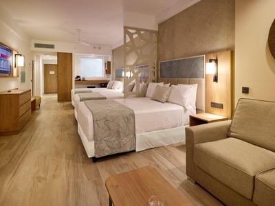 Modern furnished hotel room with a large double bed, sofa, and wooden flooring.