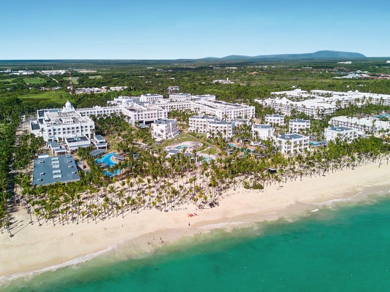 Large beach resort with pools and greenery under clear sky.
