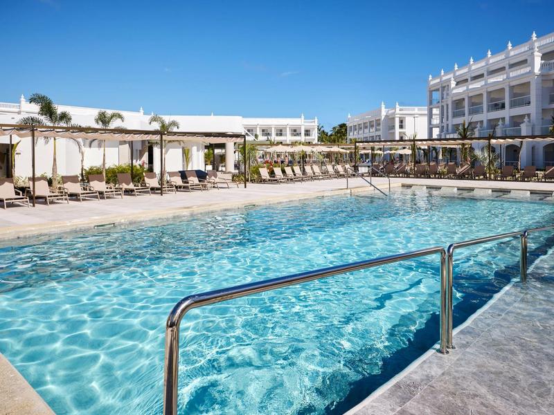 Large pool with clear blue water and surrounding loungers at a hotel.