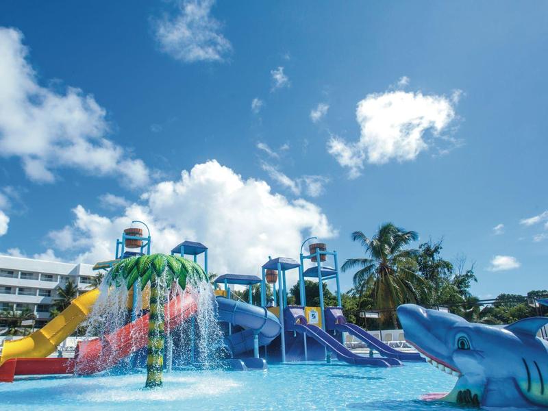 Colorful water playground with slides and water sprays in pool under blue sky.