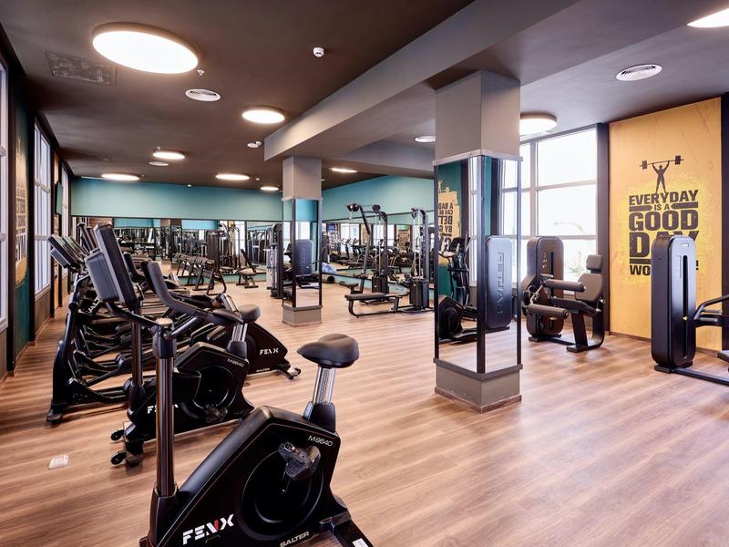 Modern gym with exercise bikes, weights, and mirrors in a hotel.