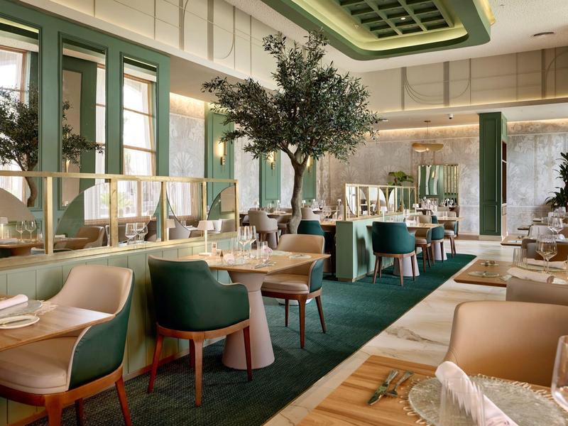 Elegant hotel restaurant with green chairs, wooden tables, and stylish lighting.