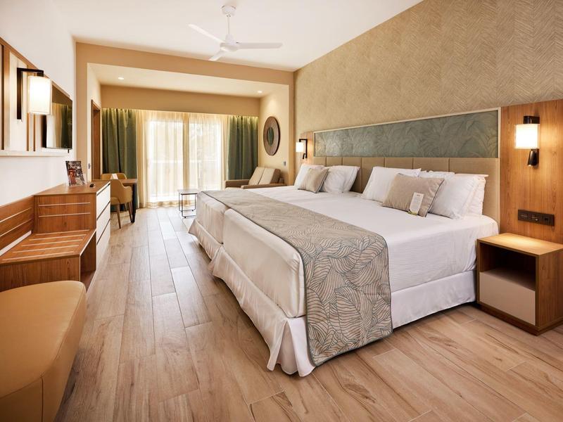 Modern hotel room with large bed, wooden furniture, and balcony with curtains.