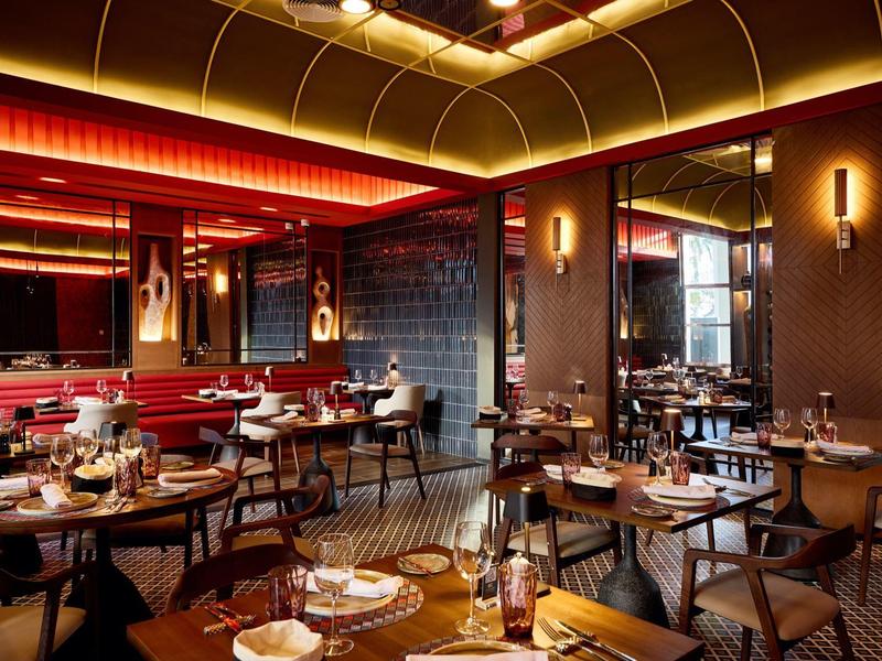 Elegant restaurant with warm lighting, wooden tables, and red upholstered seating, stylishly designed.