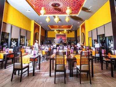 Bright restaurant with yellow walls, wooden chairs, and decorative red vases on the walls.