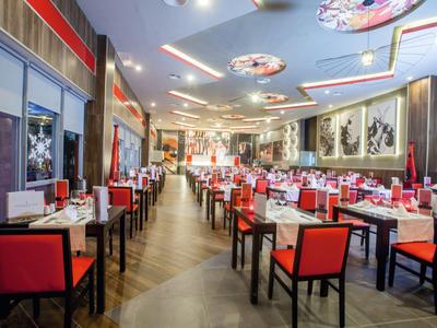 Nowoczesna restauracja z czerwonymi krzesłami i dekoracyjnym oświetleniem sufitowym.