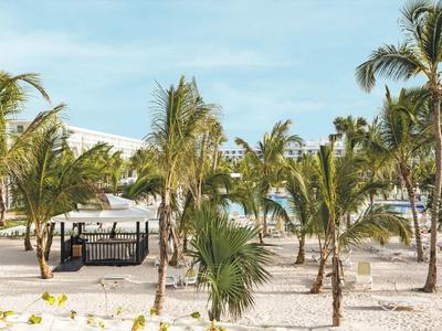Beach hotel with sand, palm trees, and lounge chairs under a blue sky.