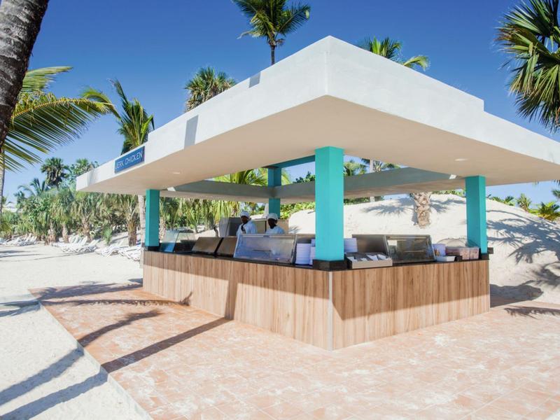 Outdoor bar with white roof and turquoise pillars on a tropical beach.