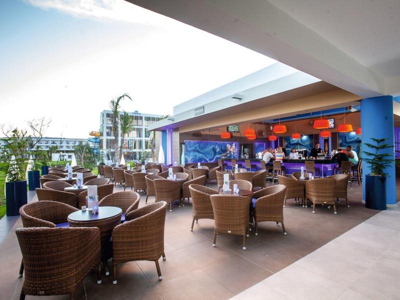 Covered hotel lounge area with wicker chairs and tables next to a green lawn.
