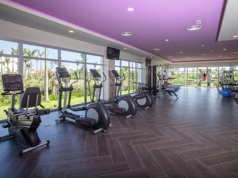 Modern gym with cardio machines and large windows overlooking a garden.