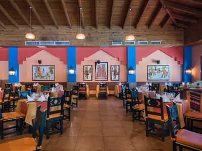 Velká restaurace s dřevěným stropem, barevnými zdmi a mnoha stoly a židlemi.