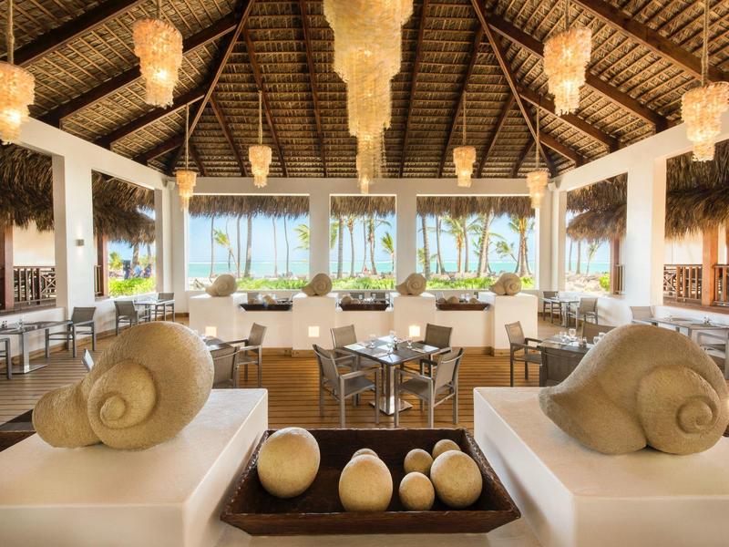 Elegantní otevřená hotelová lounge s přírodním dřevem a velkými okny s výhledem na tropickou zeleň.