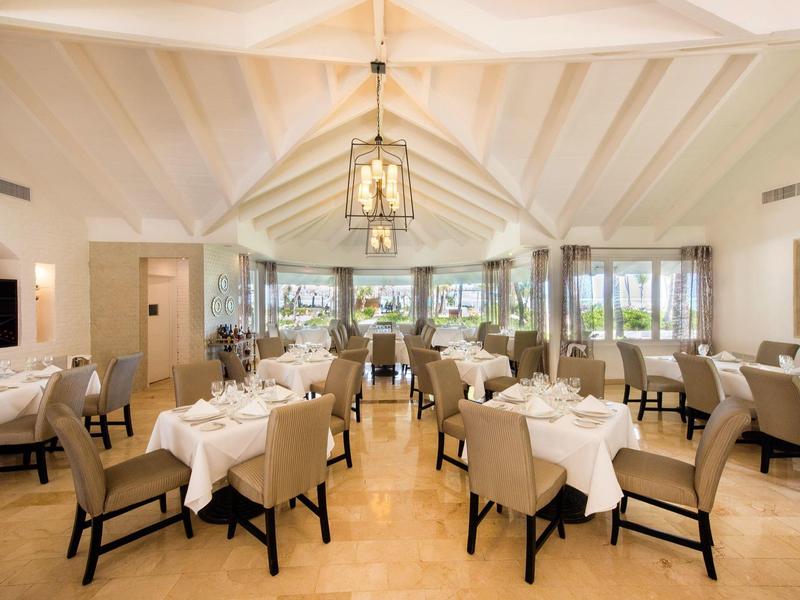 Světla, elegantní hotelová restaurace s bílými ubrusy a pohodlnými židlemi pod dřevěným stropem s trámy.