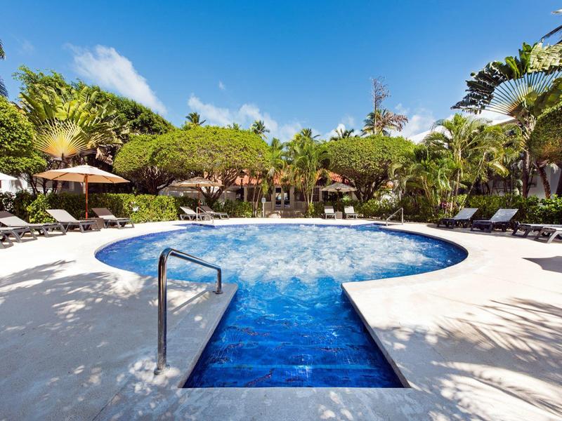 Kruhový bazén s vodopádem a lehátky v tropickém hotelovém prostředí za slunečného počasí