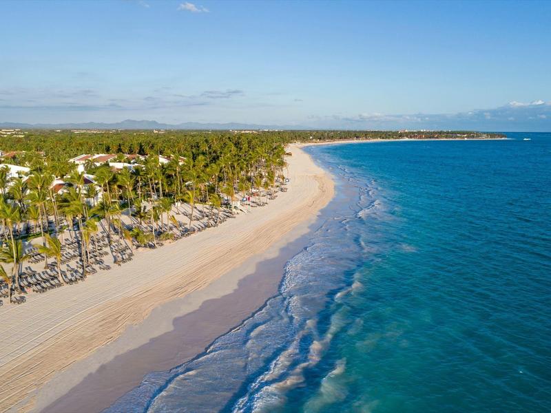 Dlouhá písečná pláž s palmami a čistou modrou vodou pod modrou oblohou