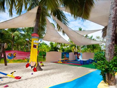 Sandy playground with shade sails and colorful games in tropical hotel setting.