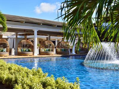 Moderní hotelový bazén s fontánou, obklopený palmami a jídelní částí.
