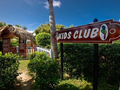 'Kids Club' sign in a lush, tropical hotel area with palm trees and clear sky.