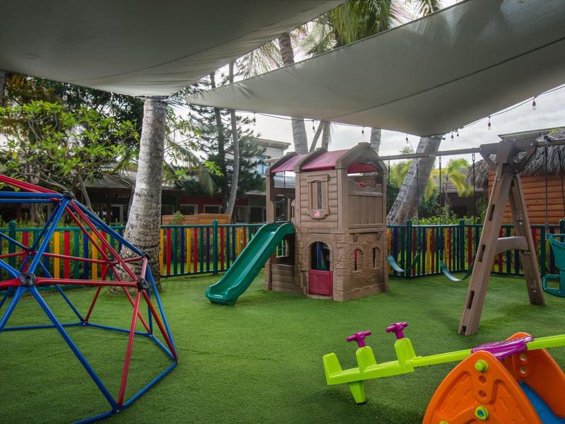 Colorful children's playground with slide, swing, climbing frame, and seesaw on green artificial turf.