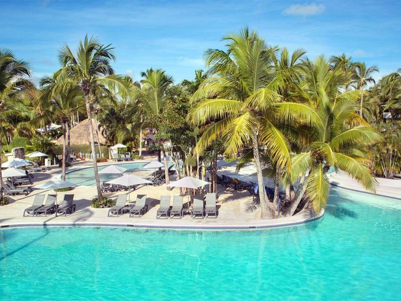 Large outdoor pool with sun loungers and palm trees in a tropical hotel resort.