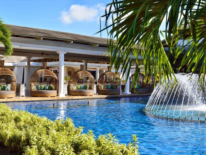 A luxurious hotel pool with large fountains, surrounded by palm trees and lounge chairs.