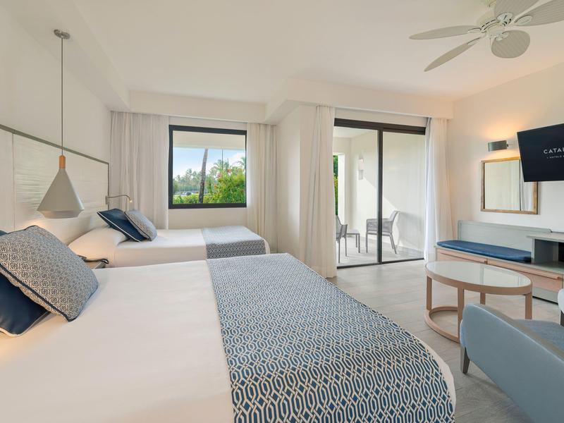 Bright hotel room with two beds, balcony, and modern decor in daylight.