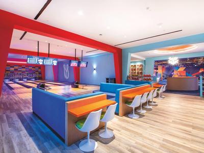 Helle, moderne Bowlingbahn mit blauen und orangen Sitzbereichen und farbigem Deckenlicht.
