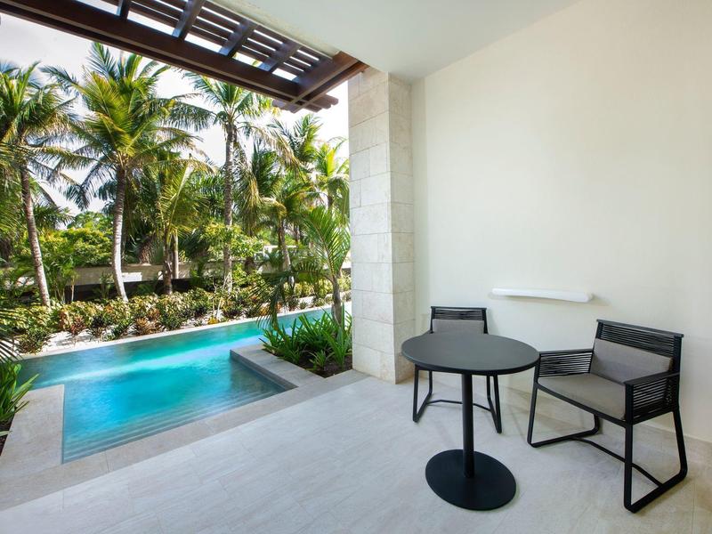 Vue sur une piscine bordée de palmiers tropicaux à côté d'une terrasse avec une table et des chaises.