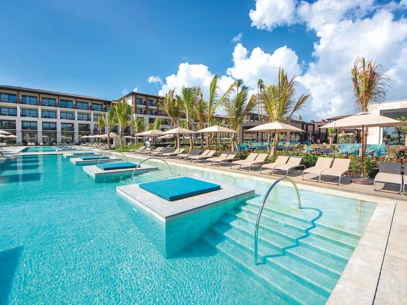 Piscine moderne d'hôtel avec transats et parasols sous un ciel bleu.