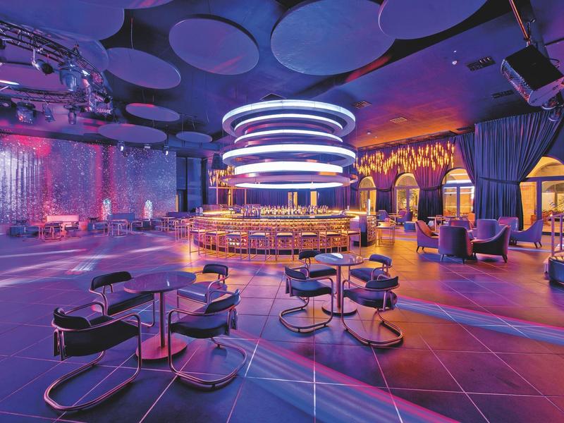 Bar moderne avec comptoir circulaire, fauteuils lounge et éclairage LED d'ambiance.