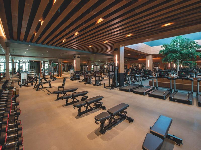 Grande salle de sport moderne avec équipements, haltères et tapis de course dans un espace lumineux.