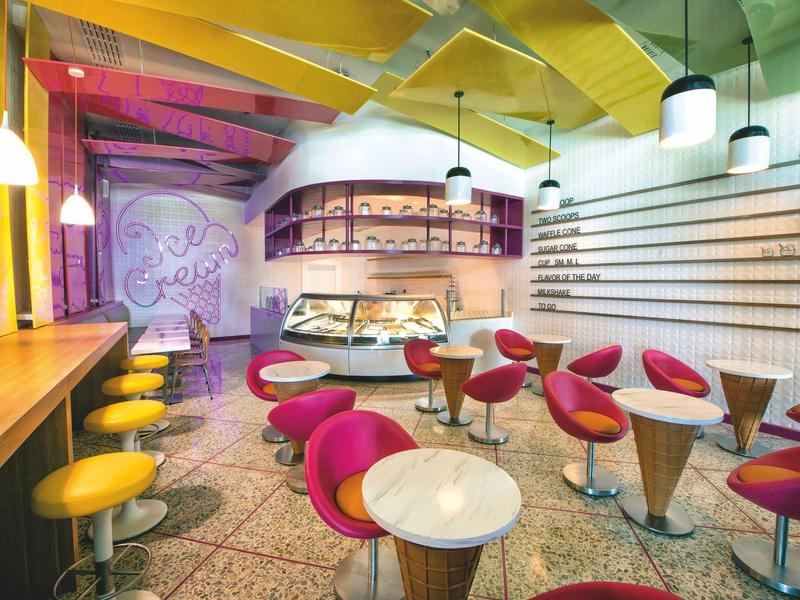 Café moderne et coloré avec des tables rondes et des chaises vives dans un cadre animé.