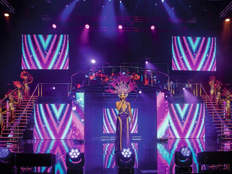 Une scène avec des écrans LED colorés et des escaliers de chaque côté, éclairée par des lumières violettes.