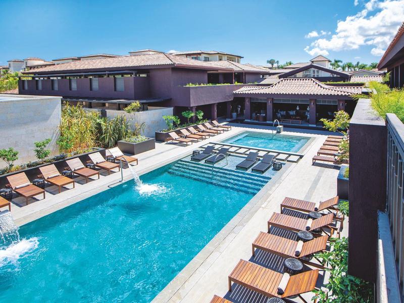 Piscine d'hôtel moderne avec chaises longues et eau claire sous un ciel bleu.