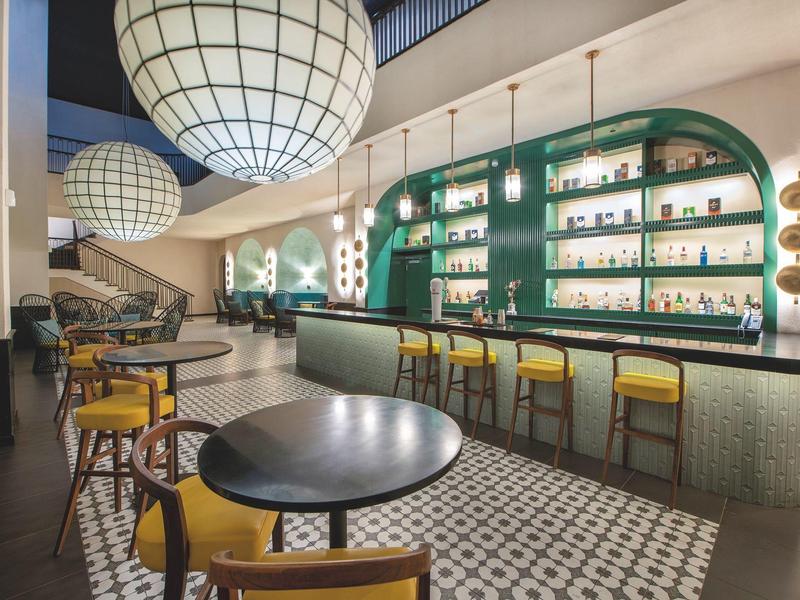 Intérieur moderne de bar d'hôtel avec table ronde noire, chaises jaunes et éclairage décoratif.