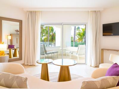 Sala luminosa con mesas redondas, sofá y puerta al balcón con vista a la piscina