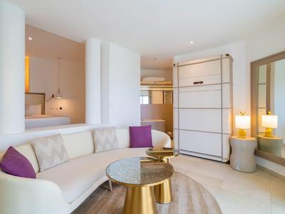 Habitación de hotel moderna con sofá curvo, cojines, espejo y mesa auxiliar elegante.