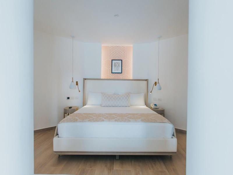 Habitación de hotel moderna con cama doble, paredes blancas y diseño minimalista.