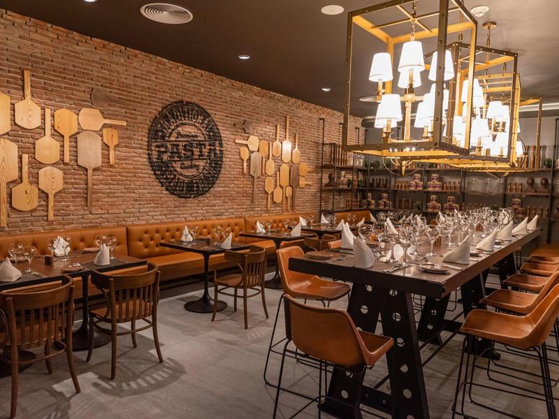 Restaurante moderno con paredes de madera, sillas de cuero y mesas servidas con luz cálida.