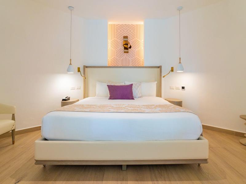 Habitación de hotel moderna con cama grande, mobiliario blanco y suelo de madera.