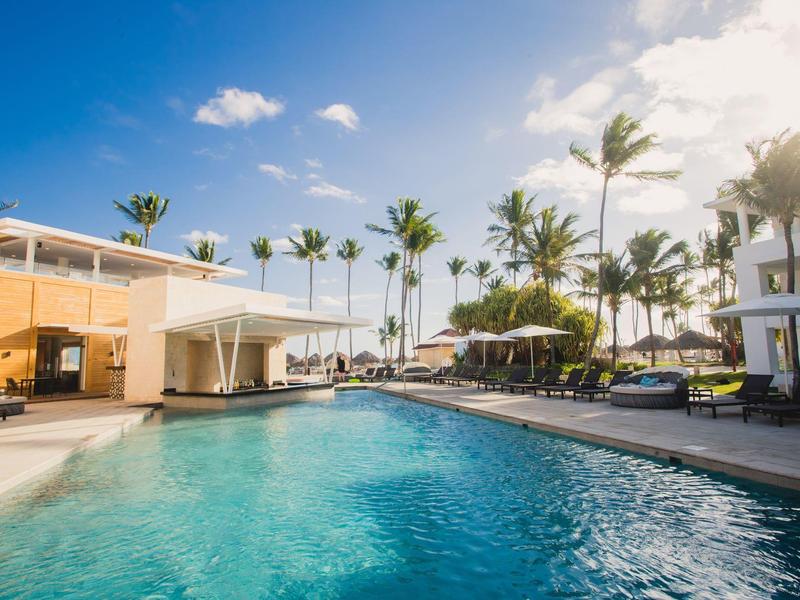 Área de piscina del hotel con tumbonas, palmeras y cielo despejado al atardecer.